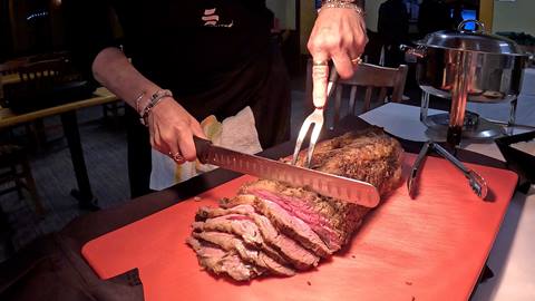 A chef uses a carving knife and fork to slice a roast of prime rib on a red cutting board at a Schweitzer banquet.
