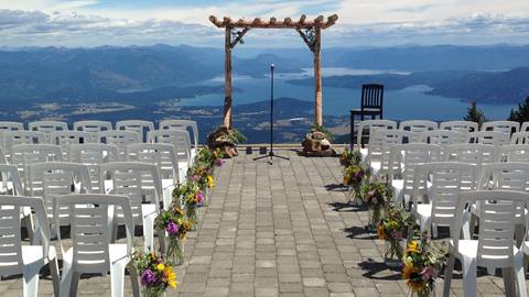 White chairs and floral arrangements line a stone-paved aisle leading to a wooden wedding arch at Schweitzer.