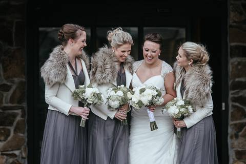 A bride and her bridesmaids laugh together while holding bouquets during a winter wedding at Schweitzer.